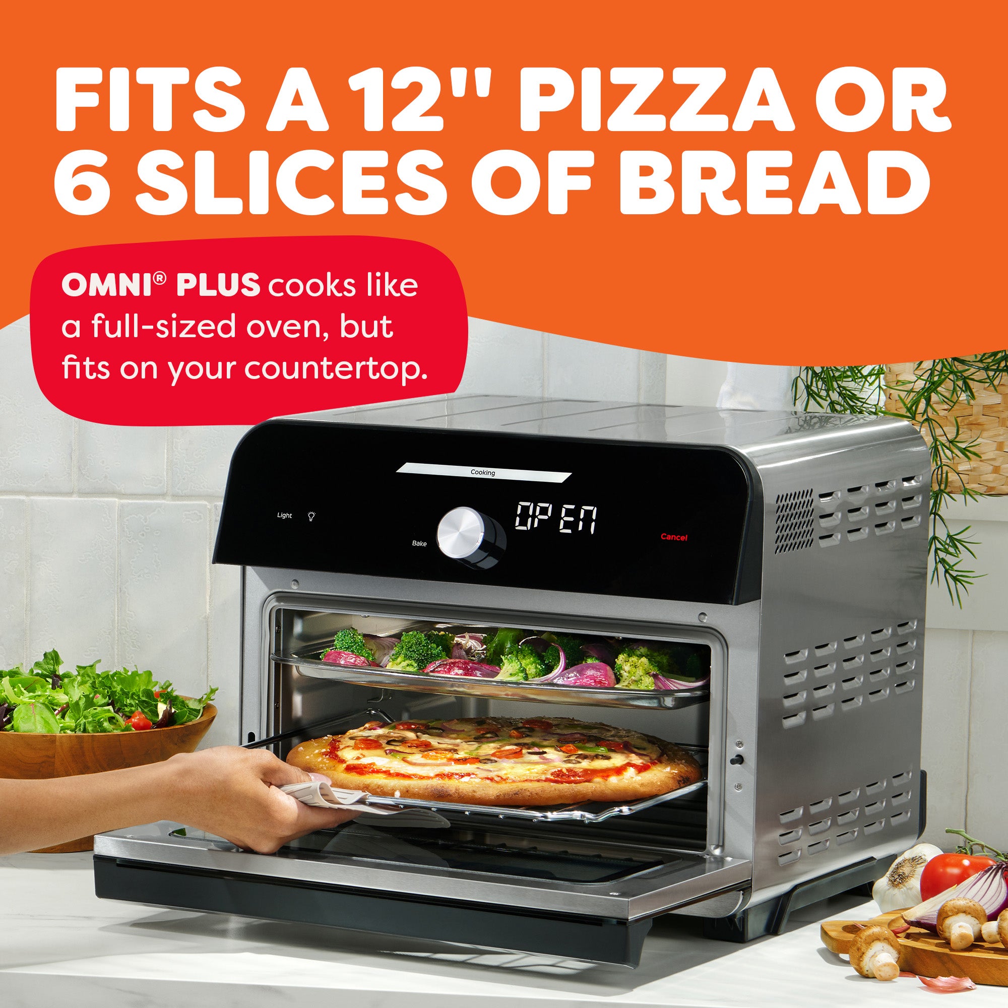 Hand placing pizza in countertop oven. Text: 'Fits a 12'' pizza or 6 slices of bread. OMNI® Plus cooks like a full oven.'