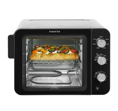 Front-facing view of the Instant Pot® 4-Slice InstantHeat™ Mini Air Fryer Toaster Oven with the door closed. A slice of focaccia bread topped with vegetables and cheese is baking on the middle rack. Manual control dials for temperature, timer, and cooking functions are on the right side of the unit.