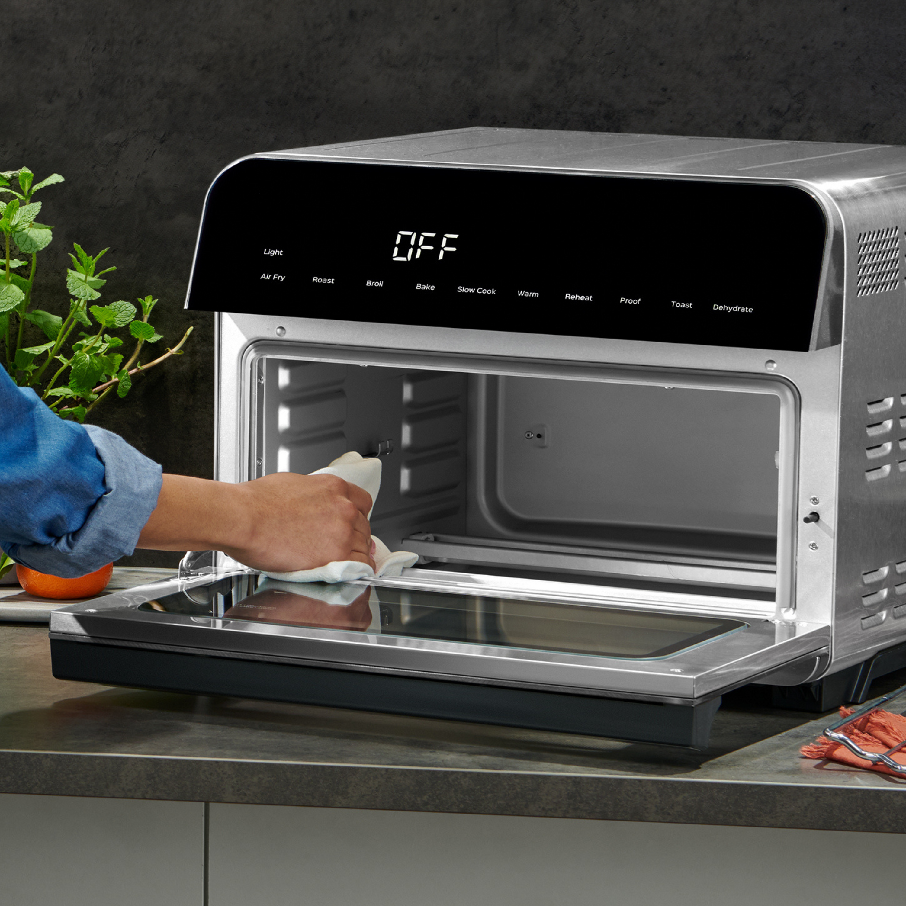Close-up of a person wiping down the inside of an open Instant Pot® toaster oven with a cloth, highlighting the easy-to-clean interior and modern digital display with various cooking functions shown on the control panel.