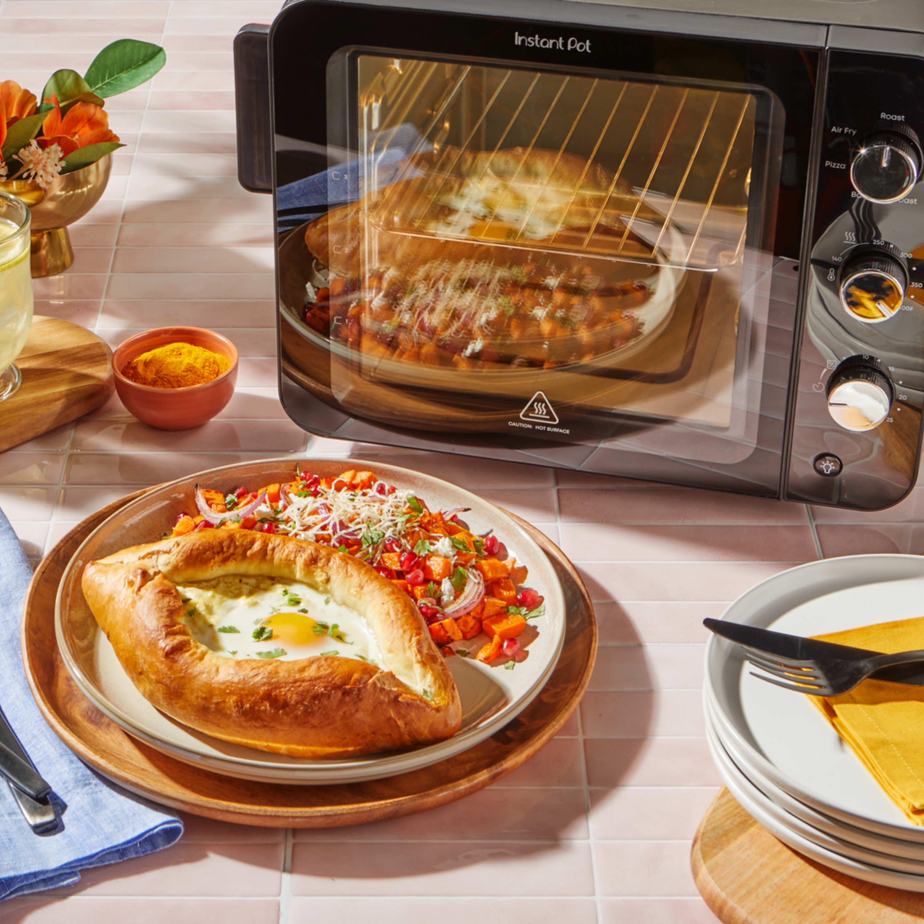 A 4-Slice InstantHeat Air Fryer Toaster Oven with its interior light on, baking flatbreads inside, set on a pink tiled kitchen counter.