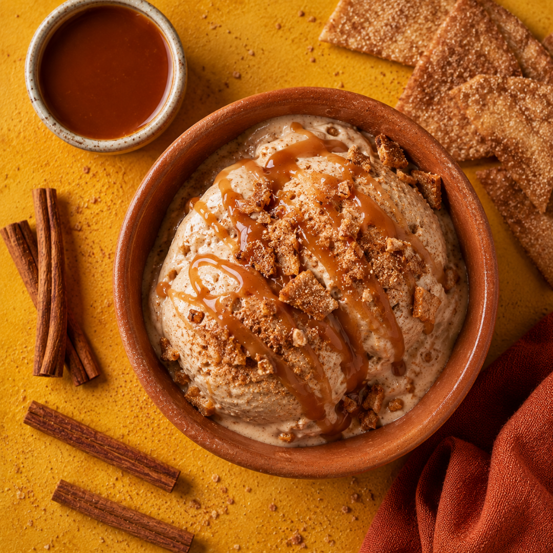 Two scoops of cinnamon churro ice cream with caramel drizzle and pita chip crumbs in a terracotta bowl on a mustard yellow background.