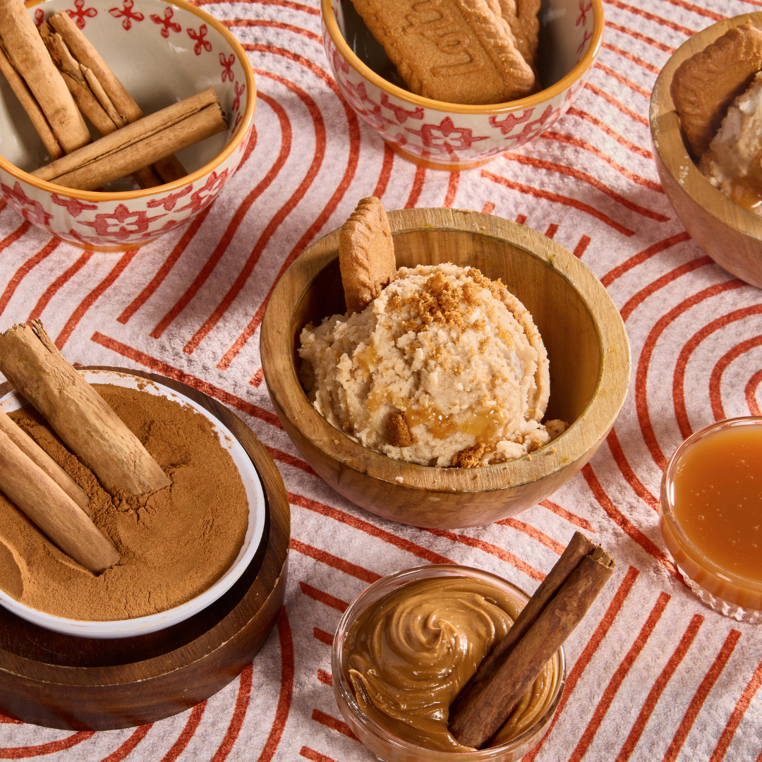 Cookie butter caramel oat milk ice cream topped with cookie crumbs and caramel drizzle, surrounded by cinnamon sticks and Biscoff cookies.