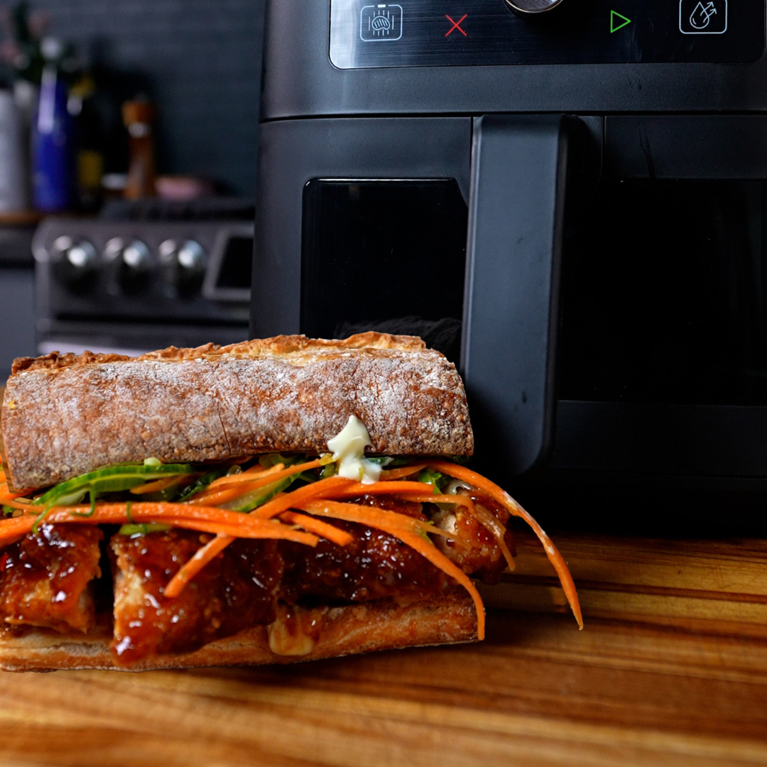 Honey BBQ chicken sandwich stacked with glazed chicken, shredded carrots, and cucumber ribbons sits in front of a black Instant Pot® 4QT Vortex® Mini Air Fryer.