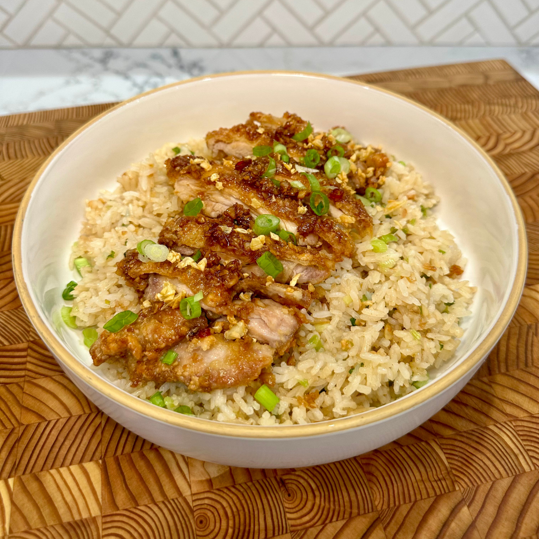 Honey garlic crispy chicken is plated over a bowl of garlic fried rice. The dish is garnished with green onions. 