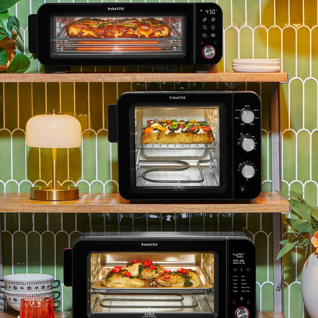 Three Instant Pot® InstantHeat™ countertop ovens displayed on wooden shelves, each cooking food inside: a pizza in the top oven, flatbread with vegetables in the middle oven, and seasoned chicken in the bottom oven, shown through illuminated glass doors.