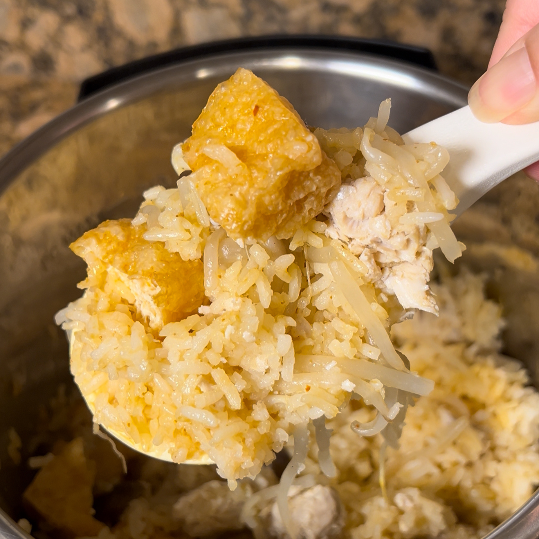 A close-up of a spoonful of Tom Yum rice held over an Instant Pot®. The rice is fluffy and golden, mixed with bean sprouts and chunks of chicken. The pot of rice is visible in the background.