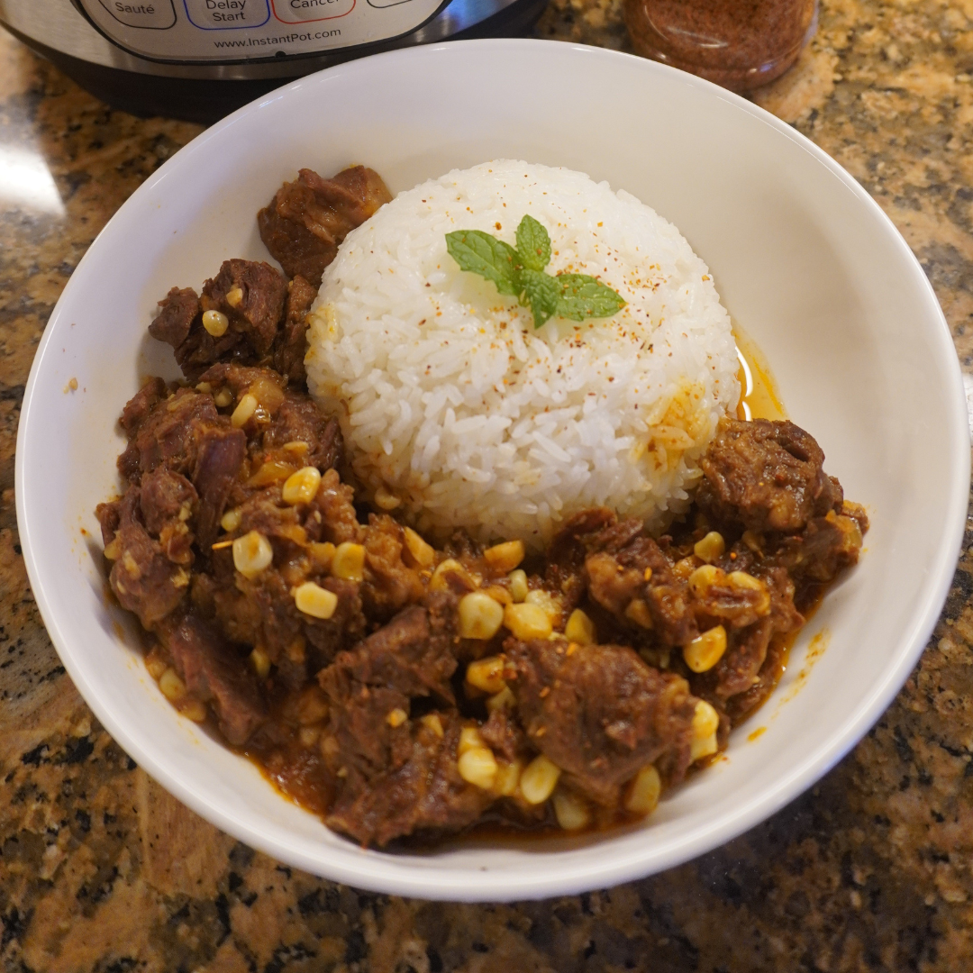 A white bowl filled with Zesty Tajín® Beef Stew served alongside a mound of white rice garnished with a small mint sprig.