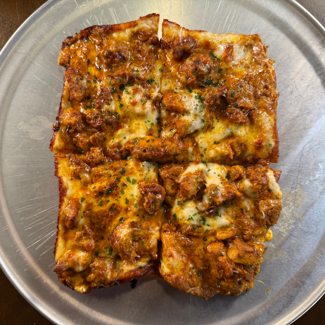 A rectangular butter chicken pizza cut into four square slices, topped with chunks of spiced chicken, melted cheese, and a sprinkle of herbs.