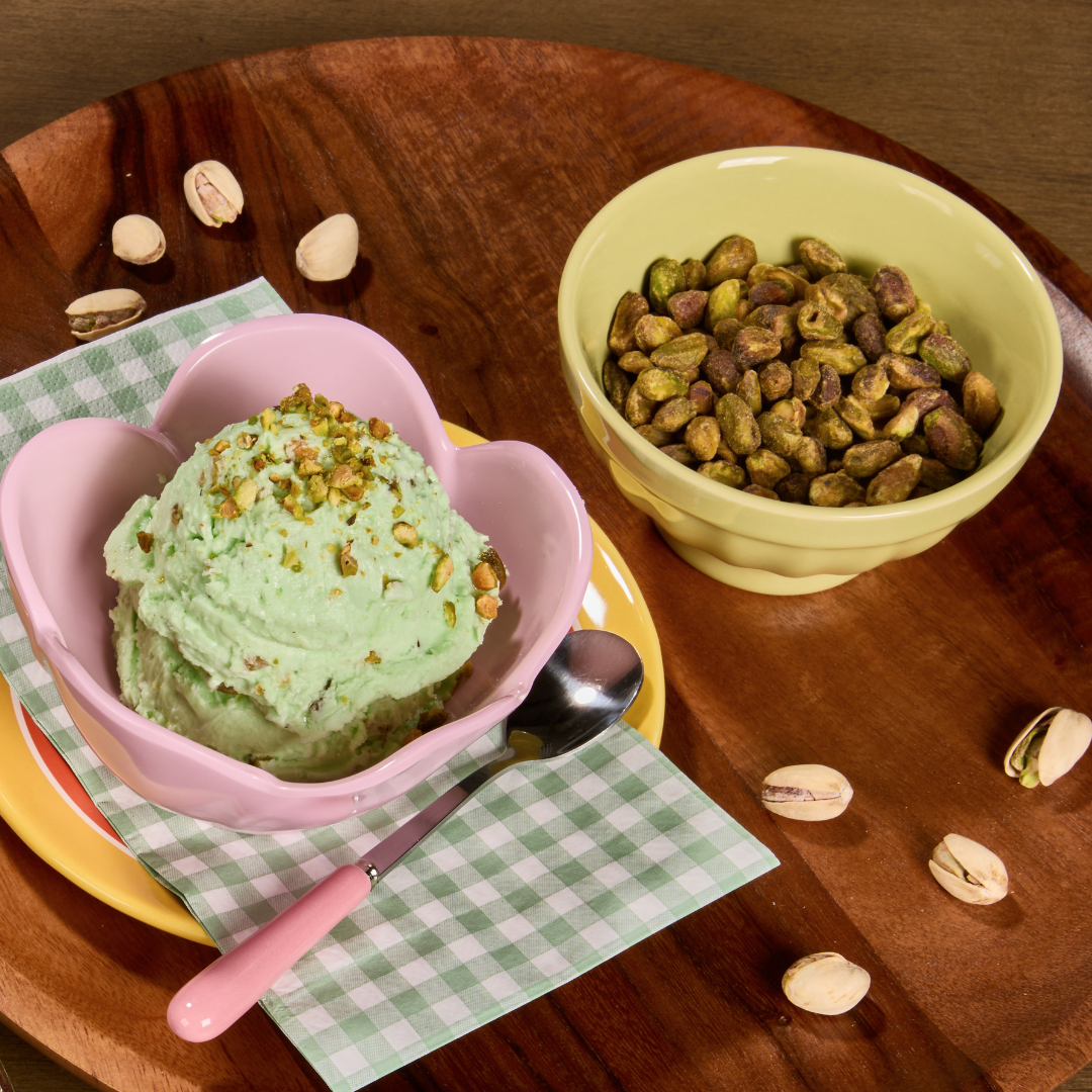 Salty pistachio gelato topped with crushed pistachios, served in a pastel dessert bowl beside roasted pistachios.