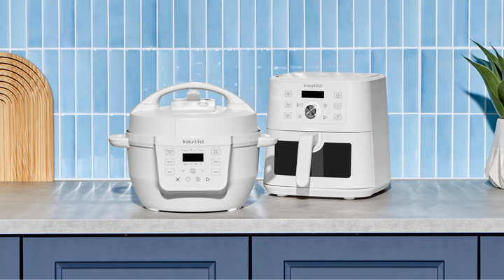 White Instant Pot® RIO™ Mini Multi-Cooker and VORTEX® Mini Air Fryer in the Sea Salt color finish, styled side by side on a kitchen counter with a blue tiled backsplash, wood cutting boards, and a green plant.