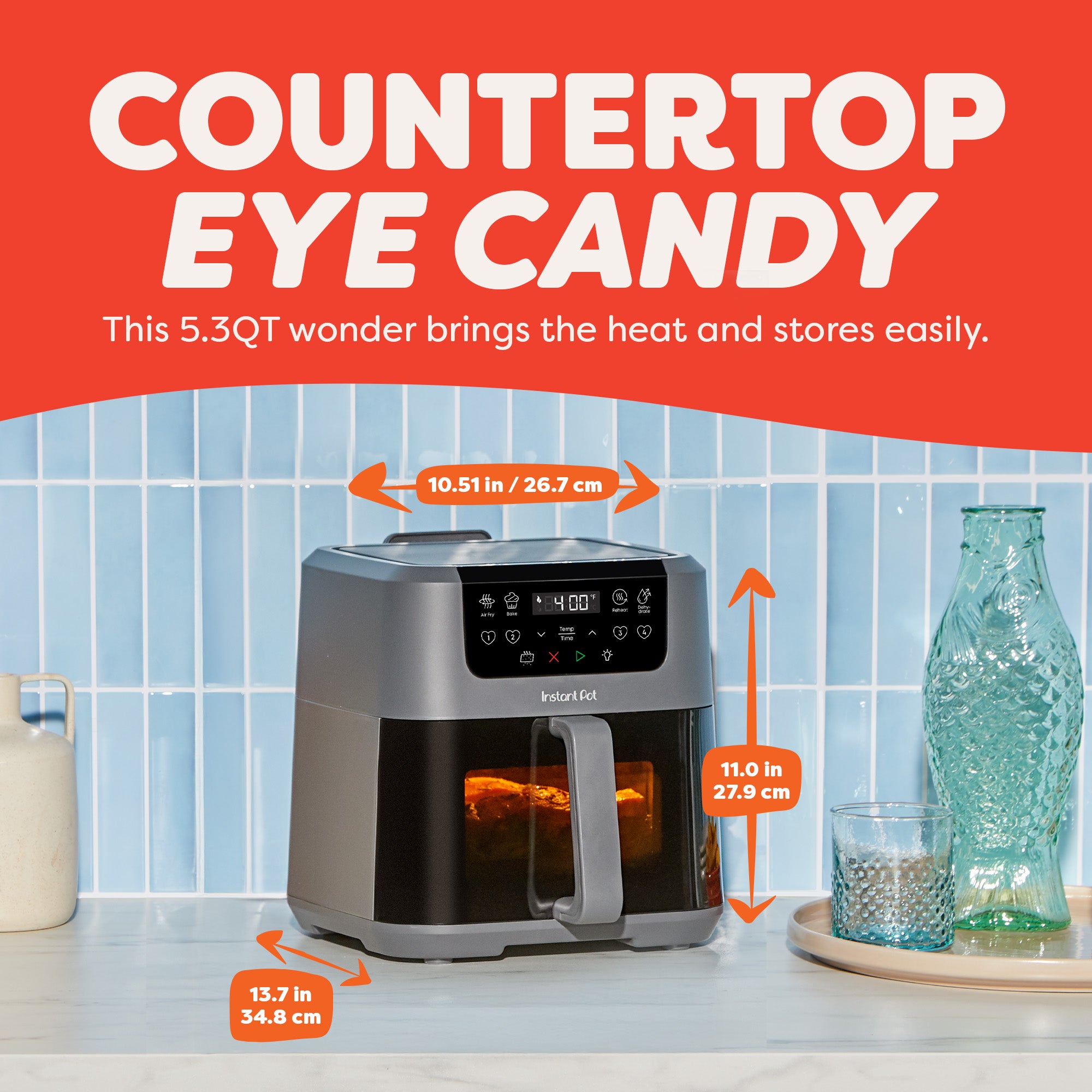The air fryer on a countertop next to a tall glass bottle and drinking glass. Measurements are labeled: 10.51 inches wide, 11 inches tall, and 13.7 inches deep. Text reads “Countertop Eye Candy.”