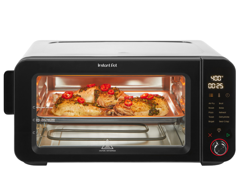 Front-facing view of the Instant Pot 6-Slice InstantHeat Air Fryer Toaster Oven with the door closed. A tray of seasoned chicken and vegetables is visible through the glass window. The digital display shows 400°F and 25 minutes. Touchscreen panel with cooking presets and control knob is on the right.