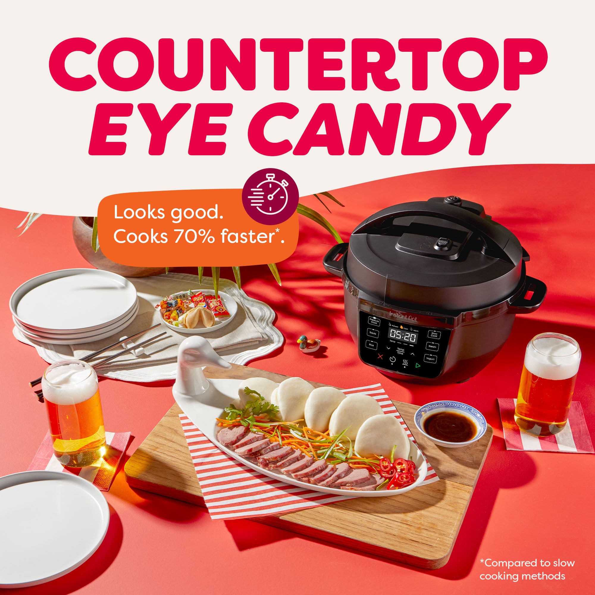 Instant Pot® 4QT RIO™ Mini Multi-Cooker in Black on a red tabletop with a tropical, playful vibe. A plate of bao buns with sliced duck, veggies, and dipping sauce sits in front, alongside beer and place settings. Text overlay says, “Looks good. Cooks 70% faster,” with the headline, “Countertop Eye Candy.”