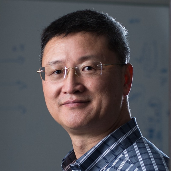 Alt text: Dr. Robert Wang, founder and inventor of Instant Pot®, smiling slightly while wearing glasses and a plaid shirt, with a softly lit background featuring faint diagrams on a whiteboard.