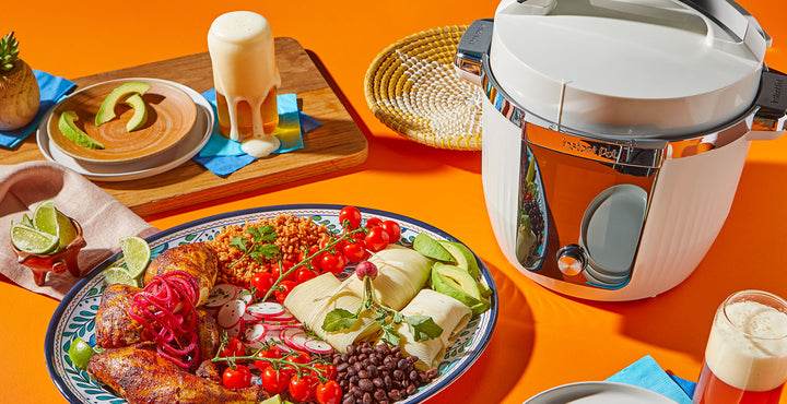 Instant Pot Pro Max sitting next to a large large plate of roasted chicken, black beans, tamales, avocado, tomatoes and radishes. Top left corner has a cutting board with a large foamy beer. 