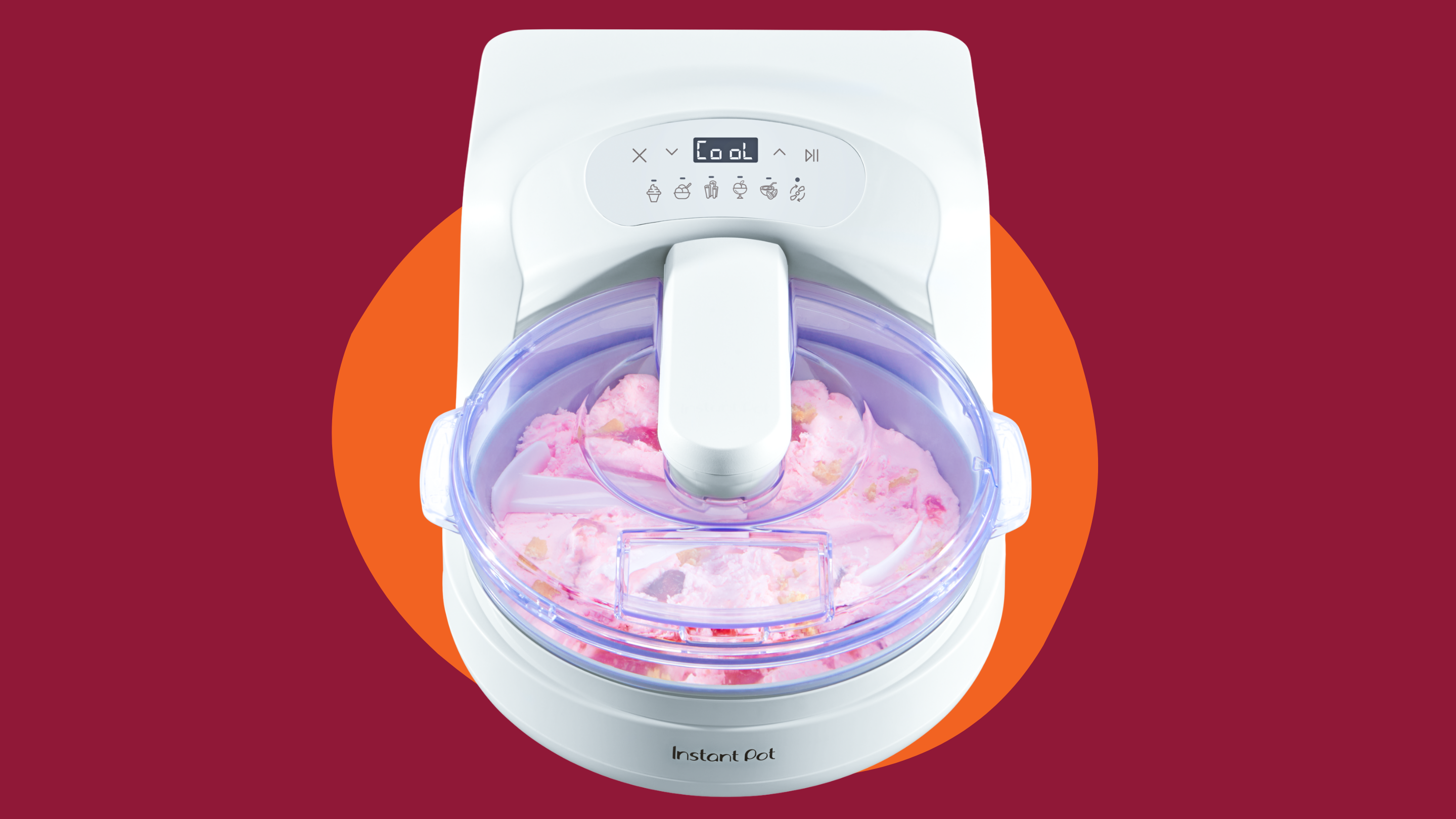 Top-down view of the white InstantChill™ ice cream maker blending pink ice cream with mix-ins inside the bowl, set against a deep berry background with a bright orange circle accent behind the appliance.
